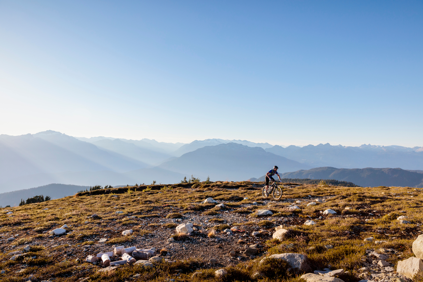 Profile silhouette of cyclist riding mountain bike on rocky hillside under mountains and clear blue sky in majestic remote landscape